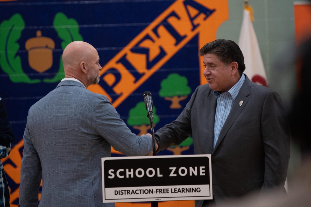 Illinois Gov. J.B. Pritzker shakes hands with Oak Park and River Forest High School Superintendent Gregory Johnson at a press conference promoting a statewide cell phone ban in schools.